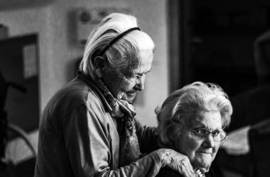 greyscale photo of woman standing behind woman sitting on chair