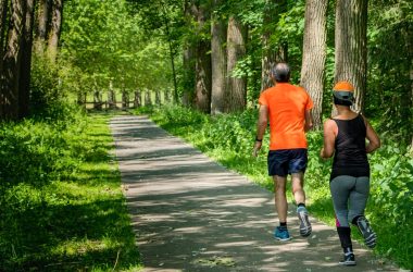 man in orange t-shirt and gray pants with blue shoes walking on pathway