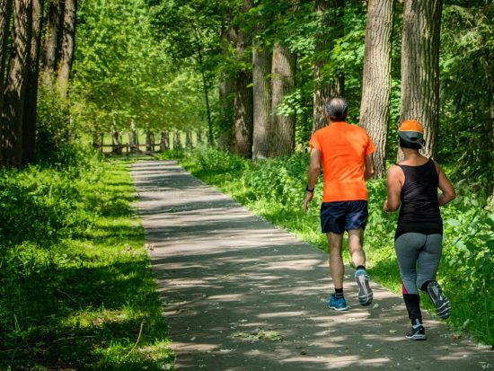 man in orange t-shirt and gray pants with blue shoes walking on pathway