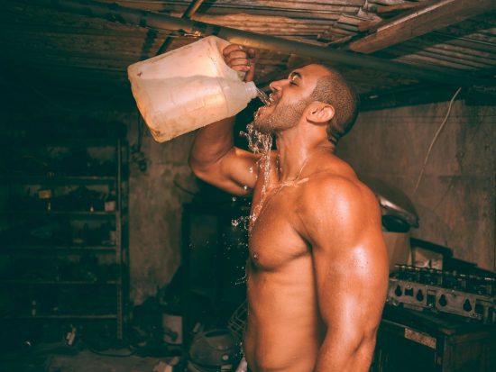 topless man drinking water from plastic container