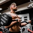 topless man in black shorts carrying black dumbbell