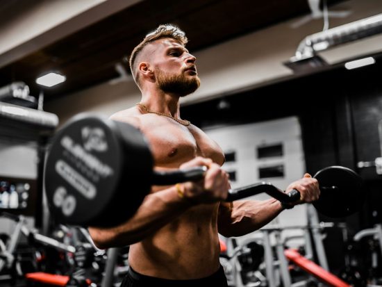 topless man in black shorts carrying black dumbbell