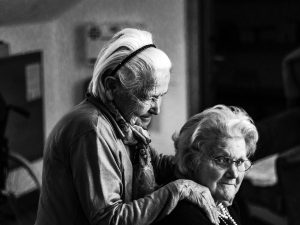 greyscale photo of woman standing behind woman sitting on chair