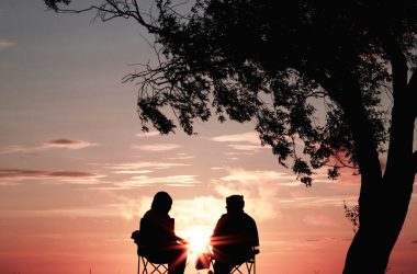 silhouette of two person sitting on chair near tree