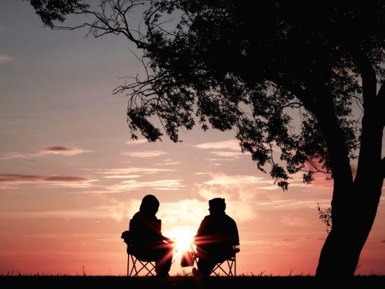 silhouette of two person sitting on chair near tree